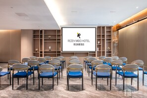 A conference room with rows of chairs, a large screen, and shelves with decorative items.