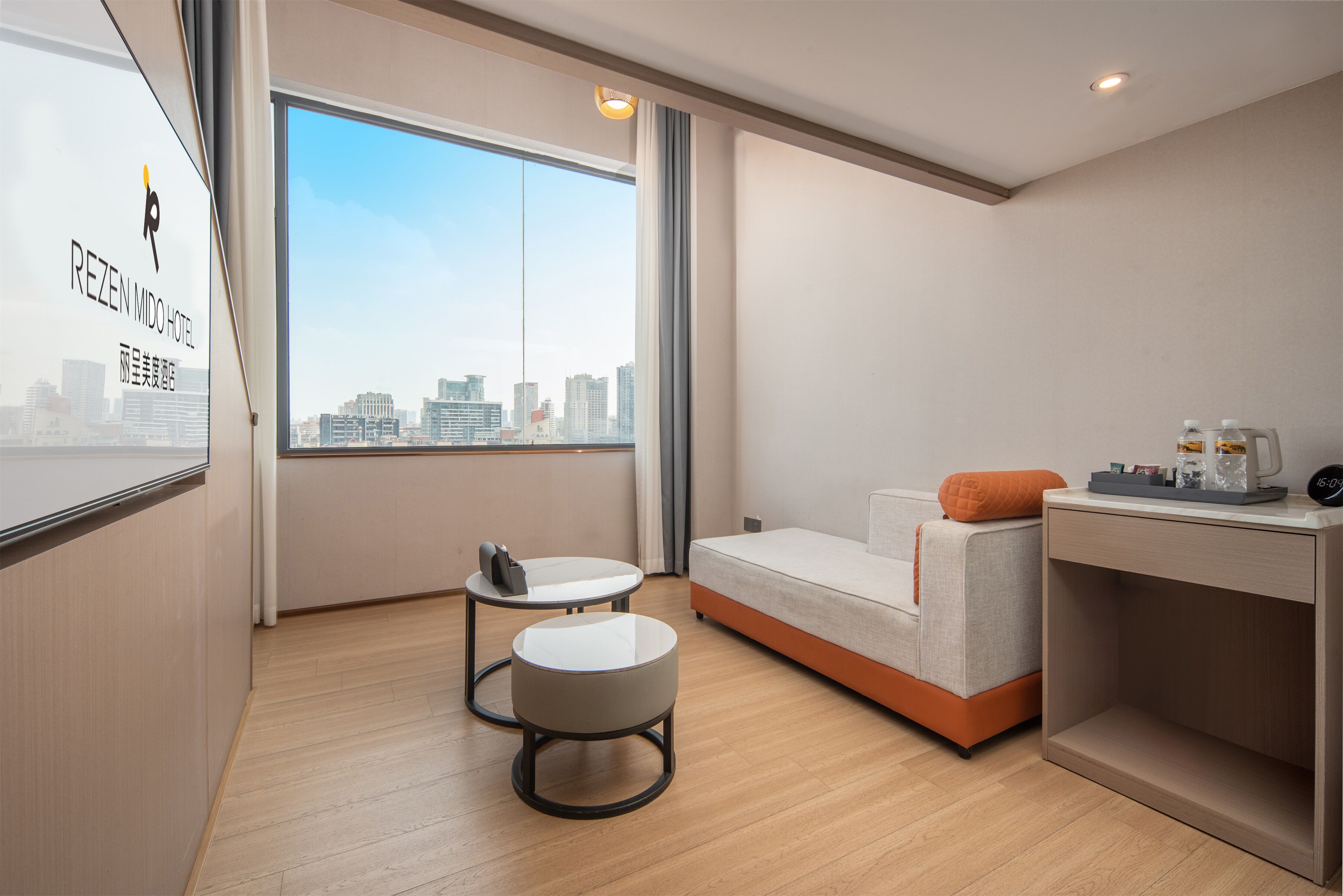 A modern hotel room with a city view, a sofa, a small table, and a desk with a chair.