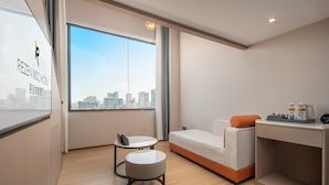 A modern hotel room with a city view, a sofa, a small table, and a desk with a chair.