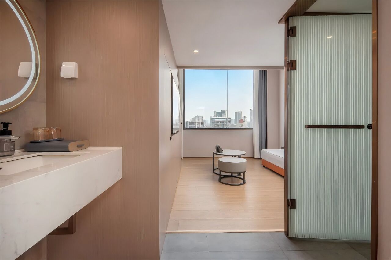 A modern bathroom with a large mirror, a white countertop, and a view of the city through large windows.