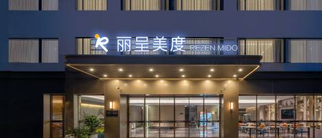 A hotel entrance with a modern facade, large windows, and a sign that reads 'REZEN MIDO'.
