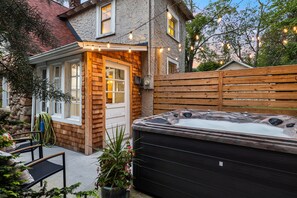 A hot tub in a backyard with a wooden fence, a stone wall, and a window overlooking the yard. - Historic cottage-Same builder as Grove Park Inn-HOT TUB-15 mins to ASHEVILLE (Swannanoa)