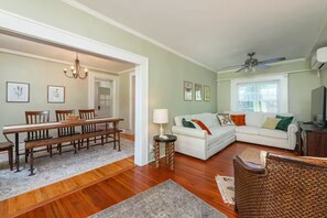A spacious living room with a dining area, a white sofa set, a chandelier, and a ceiling fan. - Historic cottage-Same builder as Grove Park Inn-HOT TUB-15 mins to ASHEVILLE (Swannanoa)