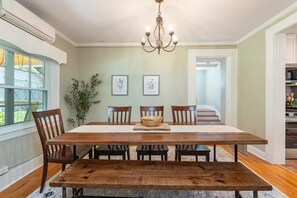 A dining room with a wooden table, chairs, a chandelier, framed botanical prints, and a view of the outdoors. - Historic cottage-Same builder as Grove Park Inn-HOT TUB-15 mins to ASHEVILLE (Swannanoa)