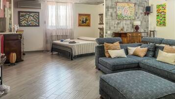 A modern living room with a sectional sofa, a bed with a striped bedspread, and a wooden floor.