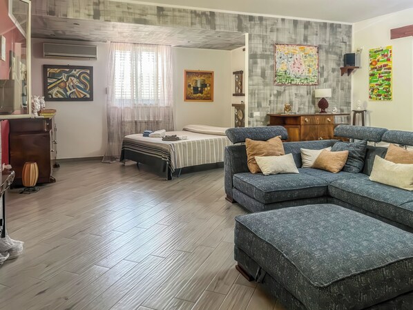 A modern living room with a sectional sofa, a bed with a striped bedspread, and a wooden floor.