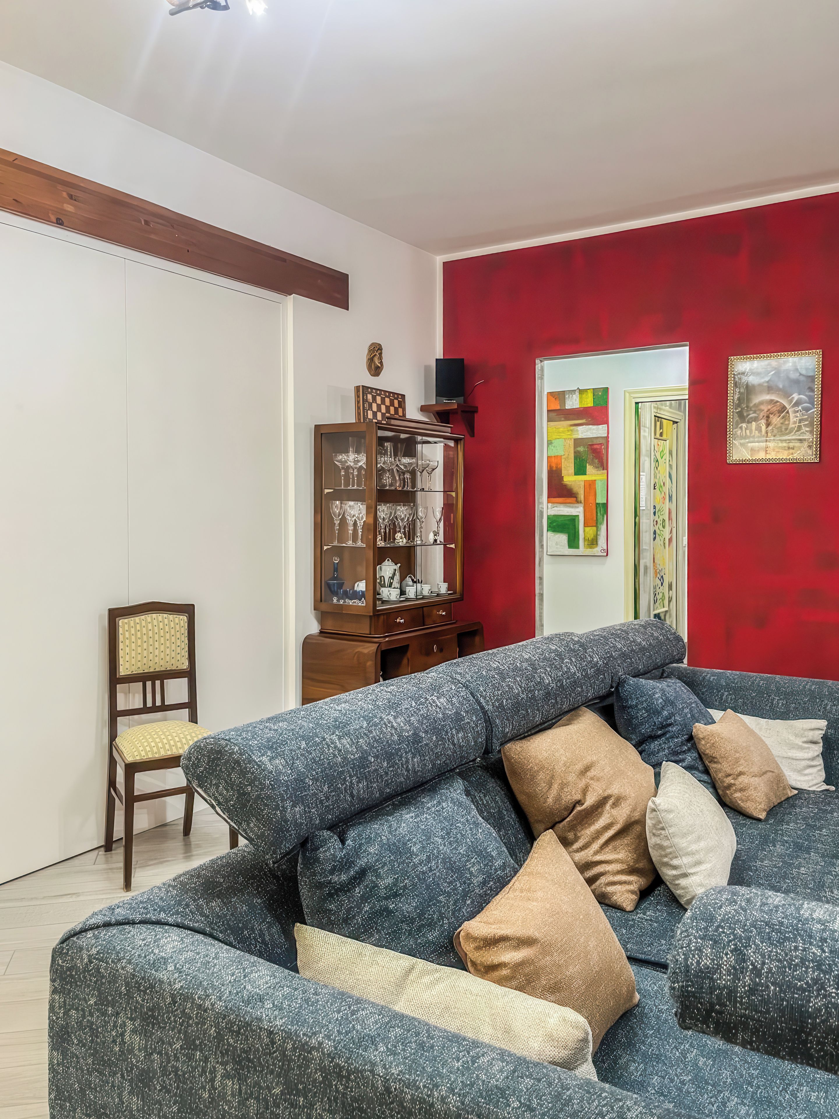 A living room with a blue sofa, a wooden cabinet with glass doors, and a red accent wall.