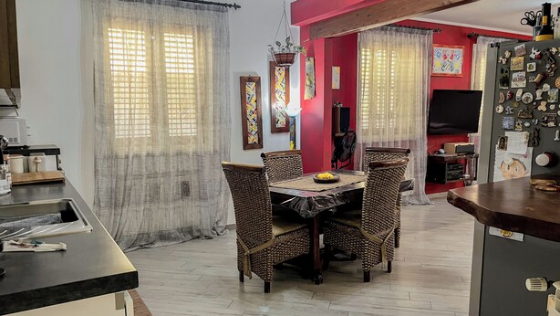 Un comedor con una mesa y sillas, una zona de cocina con un refrigerador, y una pared de acento roja.