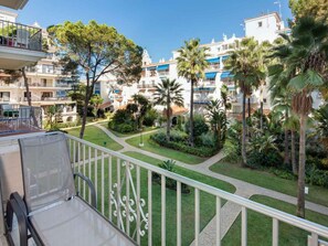 A balcony with a view of a courtyard with palm trees and a building with blue balconies. - 1 Dormitorio Andalucia del Mar Ref 209 (Marbella)