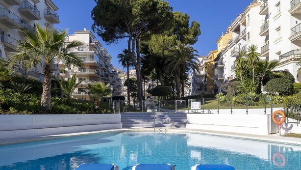 Ein Swimmingpool mit Liegestühlen, umgeben von mehrstöckigen Gebäuden und Palmen.