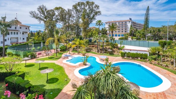 A resort with a large swimming pool, lush greenery, and a clear blue sky. - 1 Dormitorio en Medina Garden Ref 712 (Marbella)