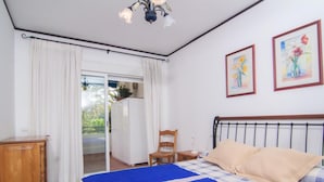 A bedroom with a bed, a wooden nightstand, a chair, a wardrobe, and a window with curtains. - 1 Dormitorio en Medina Garden Ref 712 (Marbella)