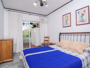 A bedroom with a bed, a wooden nightstand, a chair, a wardrobe, and a window with curtains. - 1 Dormitorio en Medina Garden Ref 712 (Marbella)