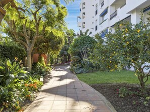 A pathway flanked by lush greenery and a white building with balconies. - 1 Dormitorio en Medina Garden Ref 712 (Marbella)