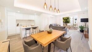 Ein modernes Interieur mit einem Holztisch, grau gepolsterten Stühlen, einer Küche mit weißen Schränken und einem Balkon mit Blick.