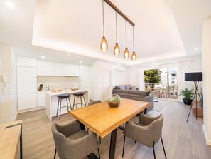 A modern interior with a wooden dining table, grey upholstered chairs, a kitchen with white cabinets, and a balcony with a view. - 2 Dormitorios Andaluc a del Mar Ref 316 (Marbella)