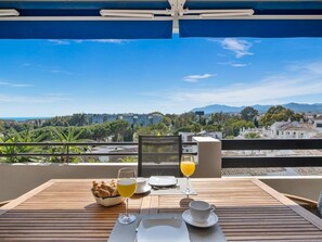 Ein Tisch ist für das Frühstück gedeckt, mit Blick auf eine Stadtlandschaft und Berge.