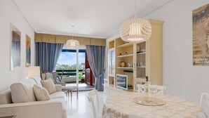 Ein modernes Wohnzimmer mit einer Couch, Sesseln, einem Esstisch mit gemustertem Tischlein und Blick durch eine Glastür auf einen Außenbereich.
