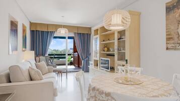 Una sala moderna con sofá, sillas, una mesa de comedor con mantel estampado y vistas a un área exterior a través de un ventanal.