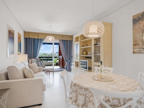 Ein modernes Wohnzimmer mit einer Couch, Sesseln, einem Esstisch mit gemustertem Tischlein und Blick durch eine Glastür auf einen Außenbereich.
