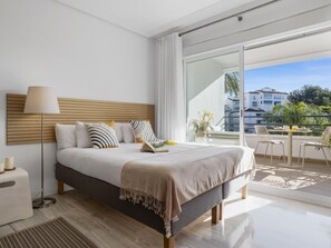 A modern bedroom with a large bed, a bedside table, a lamp, and a view of the balcony. - Acogedor Estudio en Medina Garden ref 122 (Marbella)