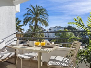 A balcony with a table, chairs, and a view of palm trees and buildings. - Acogedor Estudio en Medina Garden ref 122 (Marbella)