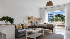 A modern hotel room with a bed, sofa, coffee table, and a balcony with a view. - Acogedor Estudio en Medina Garden ref 122 (Marbella)