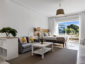 A modern hotel room with a bed, sofa, coffee table, and a balcony with a view. - Acogedor Estudio en Medina Garden ref 122 (Marbella)