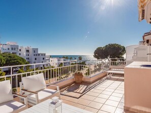 Eine Terrasse mit weißer Möbel, Blick aufs Meer und Gebäude im Hintergrund.