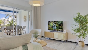 A modern living room with a sofa, a television, a coffee table, and a large window overlooking a balcony. - 2 Dormitorios en Medina Garden Ref 711 (Marbella)