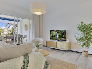 A modern living room with a sofa, a television, a coffee table, and a large window overlooking a balcony. - 2 Dormitorios en Medina Garden Ref 711 (Marbella)