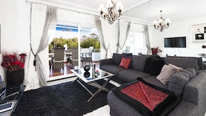 A modern living room with a grey sofa, black and red patterned throw, a glass coffee table, and a chandelier. - 2 Dormitorios Medina Garden Ref 623 (Marbella)