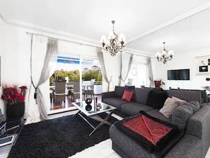 A modern living room with a grey sofa, black and red patterned throw, a glass coffee table, and a chandelier. - 2 Dormitorios Medina Garden Ref 623 (Marbella)