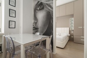 A modern room with a white bed, a dining table with clear chairs, and a large wall mural. - GuestHost - Cozy Apartment in Darsena, Near the Navigli (Milan)