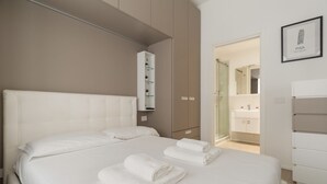 A hotel room with a bed, a white wardrobe, a bathroom visible through a glass door, and a framed picture on the wall. - GuestHost - Cozy Apartment in Darsena, Near the Navigli (Milan)