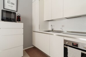 A modern kitchen with white cabinetry, a microwave, a red kettle, a sink, and an oven. - GuestHost - Cozy Apartment in Darsena, Near the Navigli (Milan)