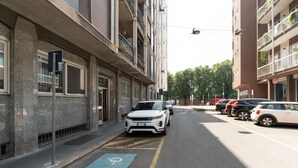 A street view with a white car parked on the side, a blue disabled parking space, and buildings with balconies. - GuestHost - Cozy Apartment in Darsena, Near the Navigli (Milan)