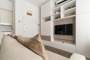 A modern living room with a sofa, a flat-screen TV, built-in shelving, and a door with a sign. - GuestHost - Cozy Apartment in Darsena, Near the Navigli (Milan)