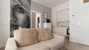 A living room with a sofa, a kitchen area, and a door. - GuestHost - Cozy Apartment in Darsena, Near the Navigli (Milan)