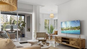 Uma sala de estar moderna com televisão de tela plana, um sofá, uma mesa de centro e uma área de jantar com cadeiras e uma mesa.