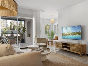 A modern living room with a flat-screen TV, a sofa, a coffee table, and a dining area with chairs and a table. - Apartamento en Medina Garden Ref 611 (Marbella)