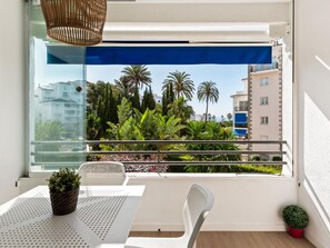 Ein Balkon mit einem weißen Tisch, zwei Stühlen, einem Korbwäschesessel und einem Blumentopf.