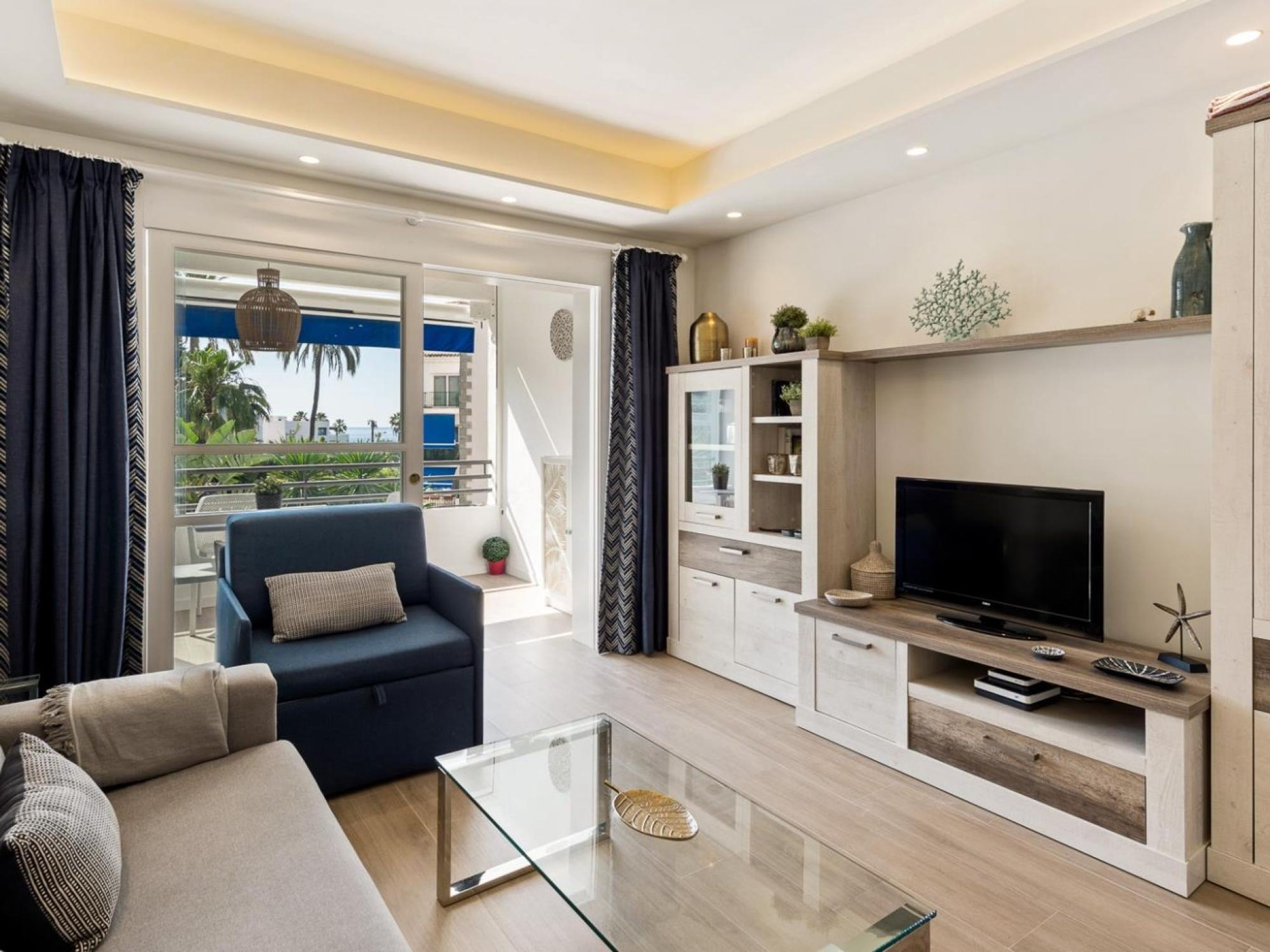 Una sala de estar moderna con sofá, televisor, una mesa de centro de vidrio y estanterías empotradas.