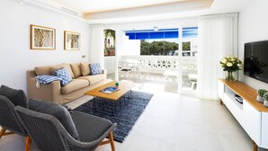 Uma sala de estar moderna com sofá, mesa de centro e cadeiras, uma televisão de tela plana e vista para o exterior.