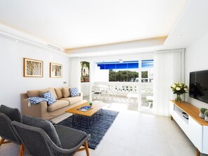 A modern living room with a sofa, coffee table, and chairs, a flat-screen TV, and a view of the outdoors. - 2 Dormitorios Casa Granada Ref 232 (Marbella)