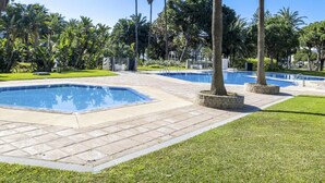 Uma área de piscina com várias piscinas, cercada por palmeiras e gramado bem cuidado.