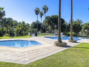 A pool area with multiple swimming pools, surrounded by palm trees and well-maintained grass. - 2 Dormitorios Casa Granada Ref 232 (Marbella)