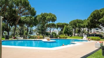 Una piscina con agua cristalina azul, rodeada de árboles y un edificio al fondo.