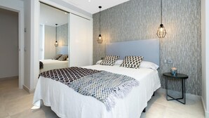 Quarto moderno com uma cama grande, duas luminárias de cabeceira, uma mesa redonda com um vaso e uma parede com textura.