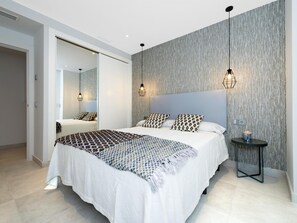 A modern bedroom with a large bed, two bedside lamps, a round table with a vase, and a textured wall. - 2 Dormitorios Casa Granada Ref 232 (Marbella)